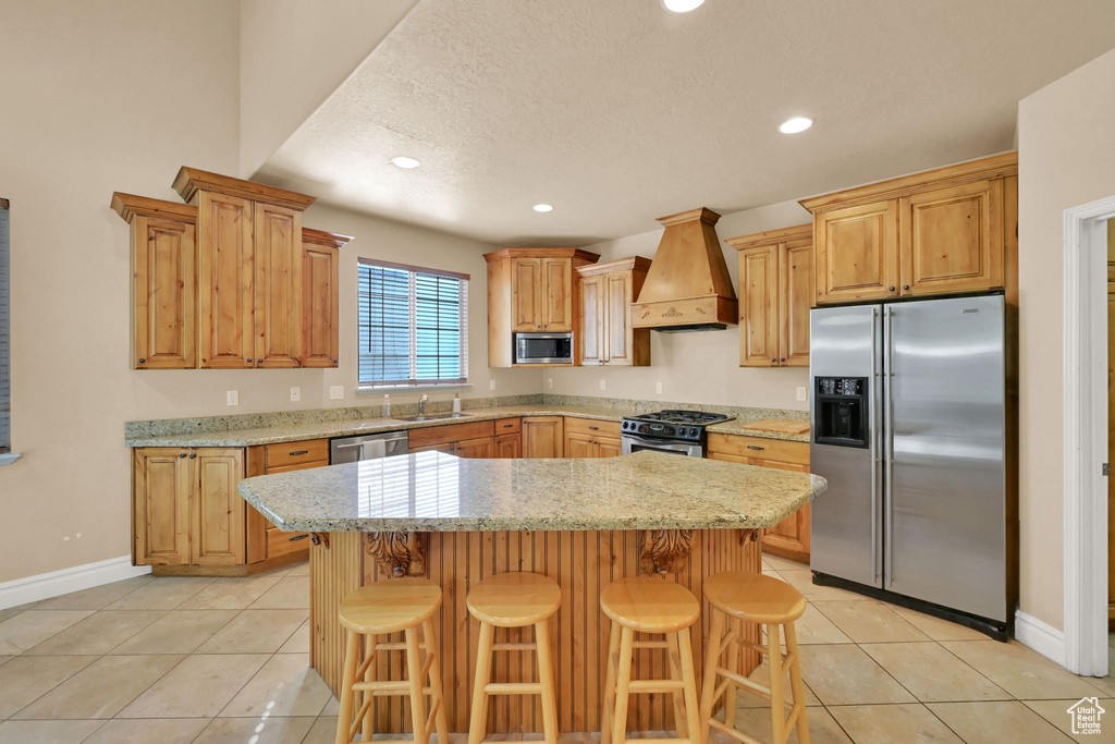 Kitchen featuring a breakfast bar, stainless steel appliances, a center island, and premium range hood