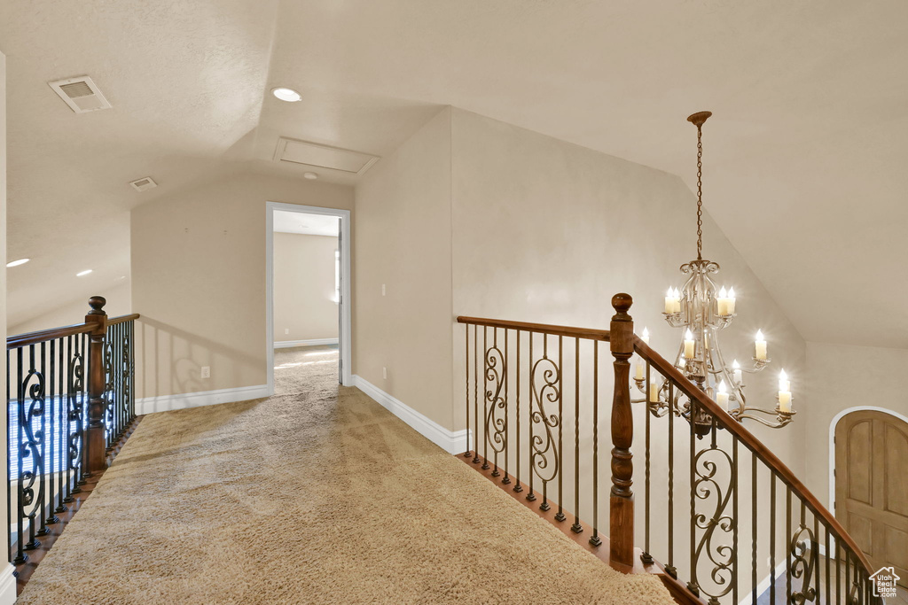 Hall featuring vaulted ceiling, carpet flooring, and an inviting chandelier