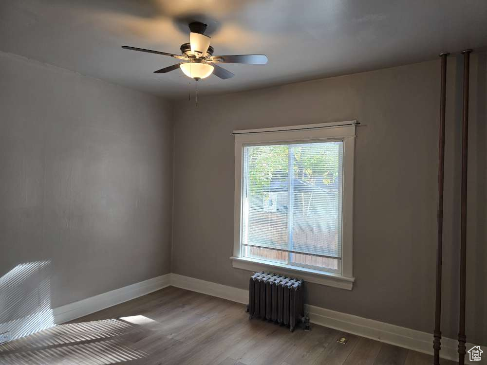 Unfurnished room featuring ceiling fan, wood-type flooring, and radiator heating unit