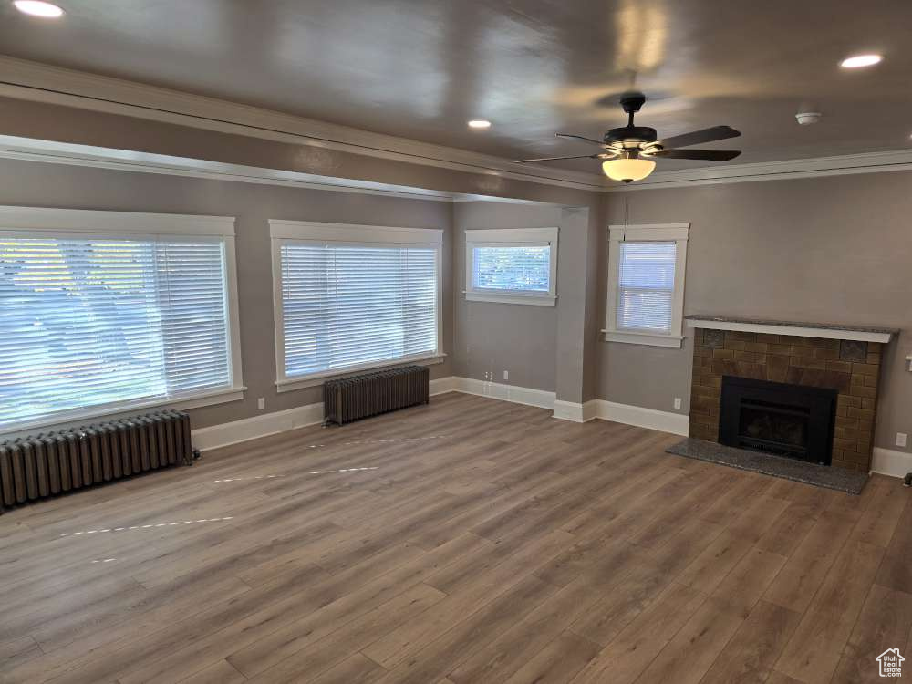 Unfurnished living room featuring radiator, ceiling fan, crown molding, and hardwood / wood-style floors