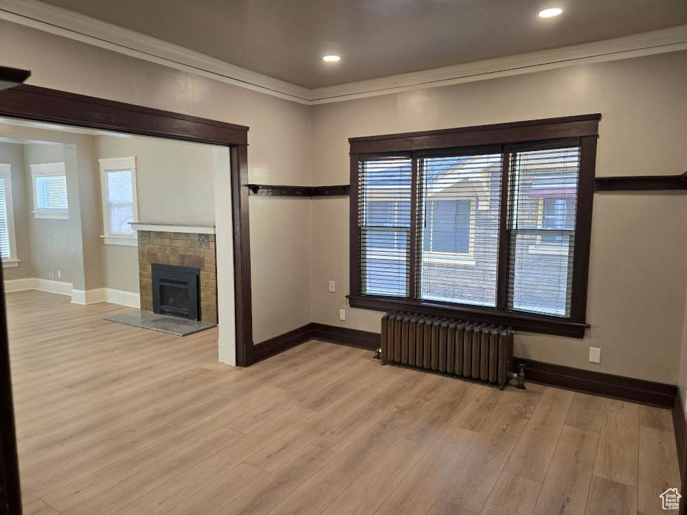 Unfurnished living room featuring light hardwood / wood-style flooring, ornamental molding, radiator heating unit, and a tile fireplace