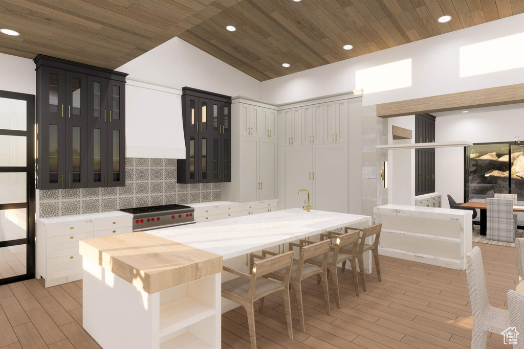 Kitchen with decorative backsplash, stainless steel stove, vaulted ceiling, white cabinets, and light hardwood / wood-style floors