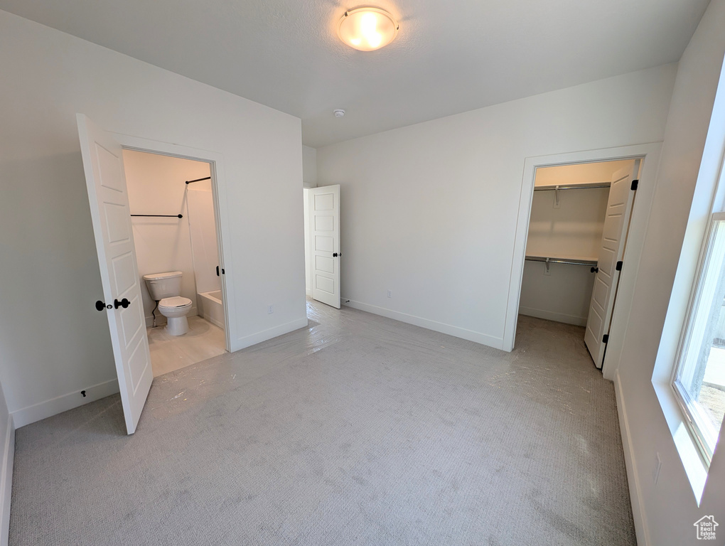 Unfurnished bedroom featuring light colored carpet, baseboards, ensuite bathroom, a spacious closet, and a closet