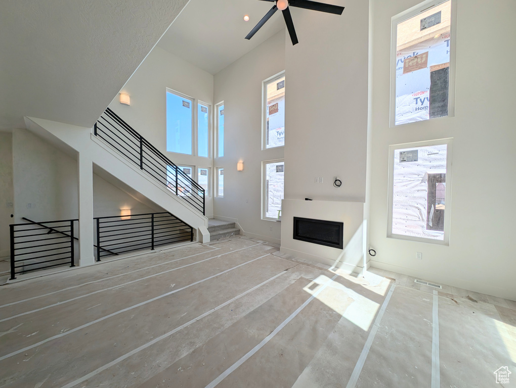 Unfurnished living room with stairs, a glass covered fireplace, a high ceiling, and ceiling fan