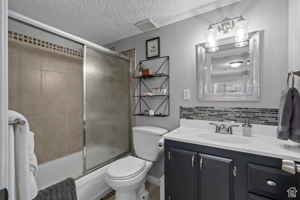 Full bathroom featuring toilet, vanity, enclosed tub / shower combo, a textured ceiling, and tasteful backsplash