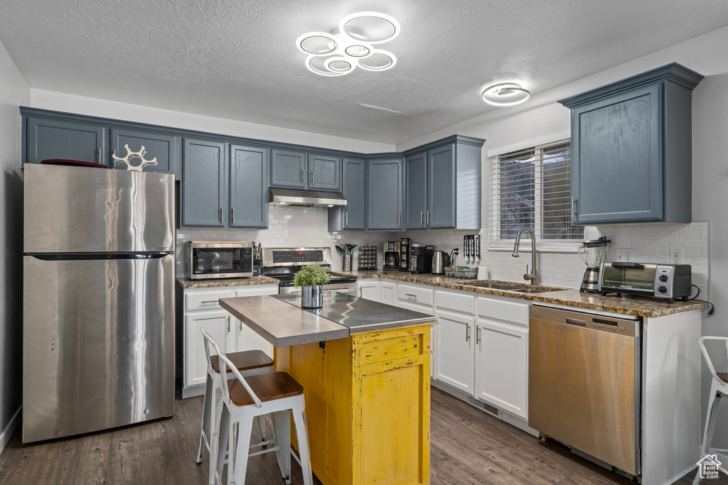 Kitchen featuring sink, a center island, white cabinetry, stainless steel appliances, and dark wood-type flooring