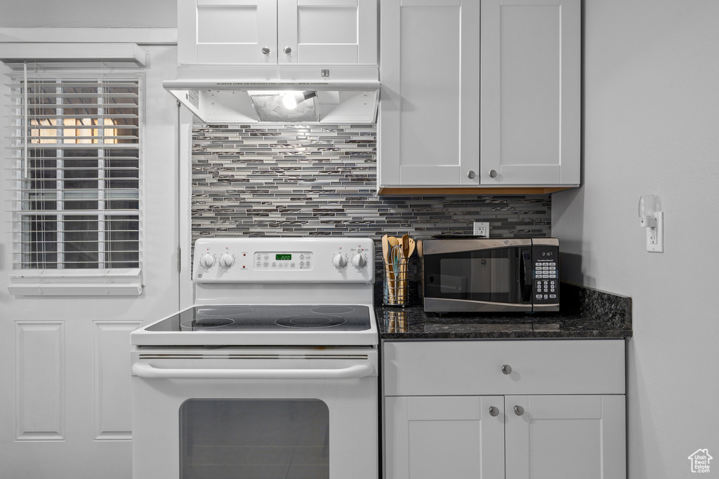 Kitchen with white range with electric stovetop, white cabinets, dark stone counters, and tasteful backsplash