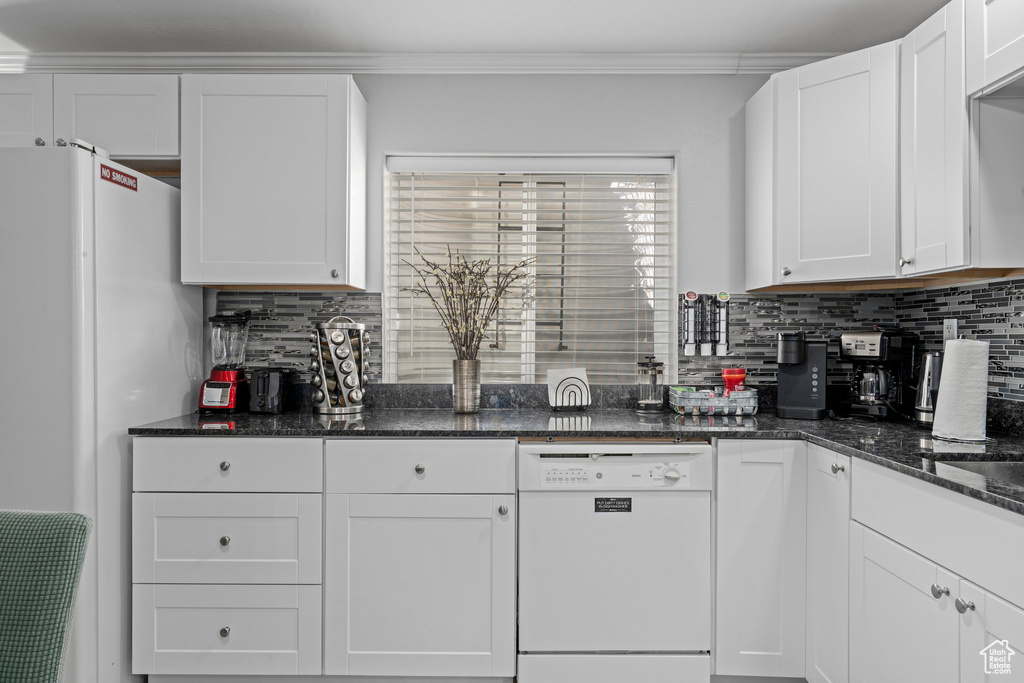 Kitchen featuring crown molding, white cabinetry, dark stone countertops, and white appliances