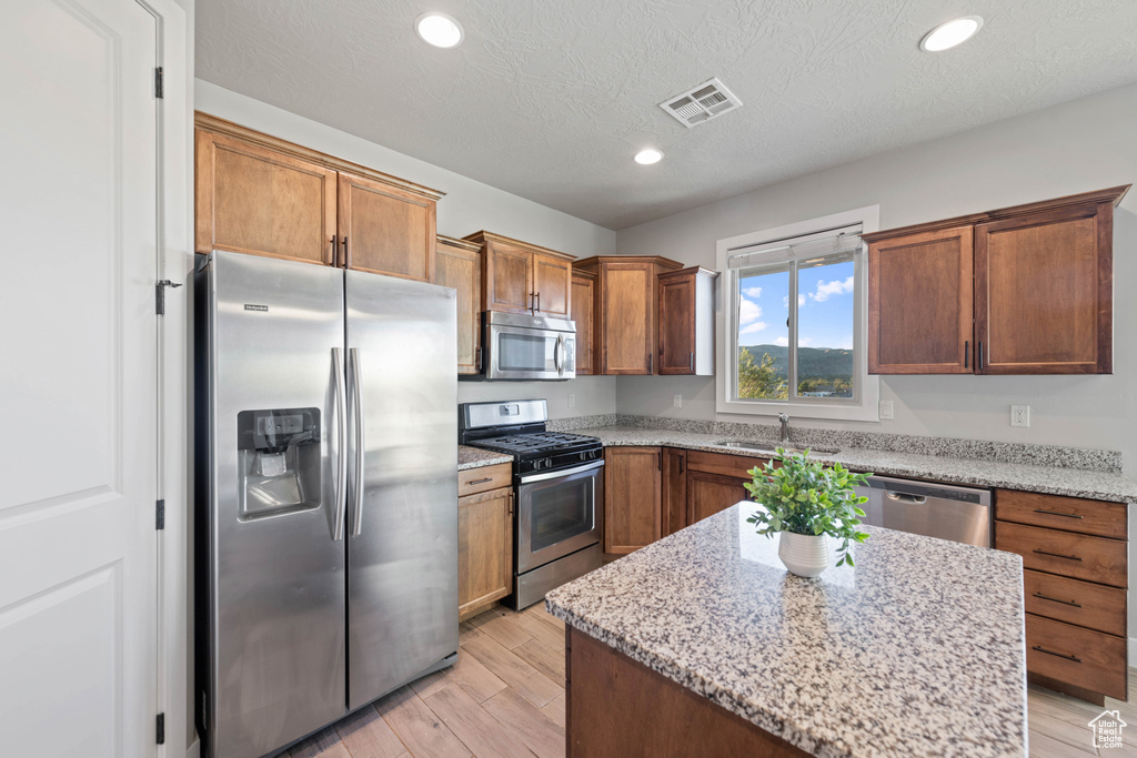 Kitchen with a kitchen island, stainless steel appliances, light stone countertops, a textured ceiling, and light hardwood / wood-style floors