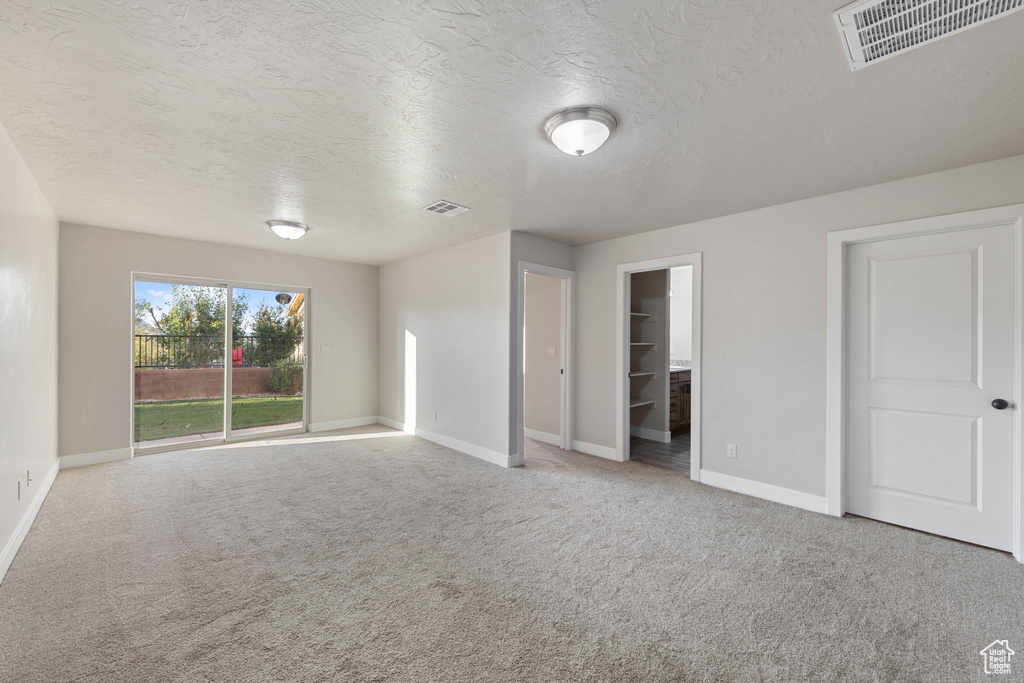 Unfurnished bedroom featuring a closet, a textured ceiling, carpet floors, and a walk in closet