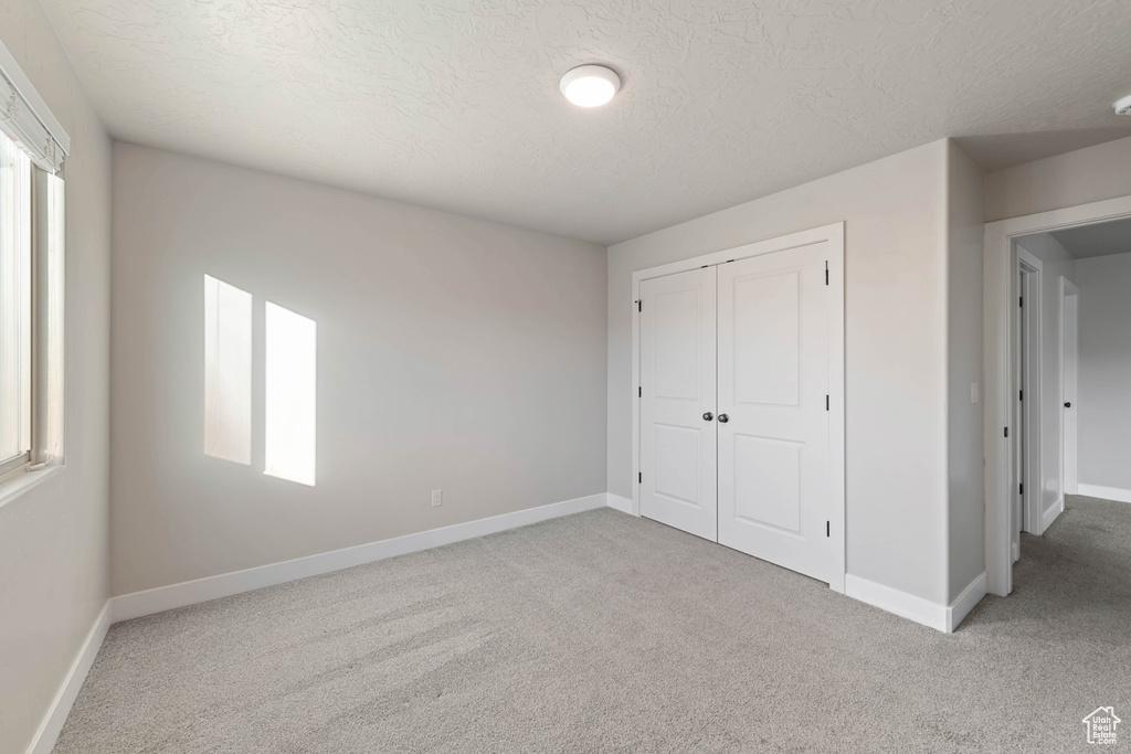 Unfurnished bedroom featuring light carpet, a textured ceiling, and a closet