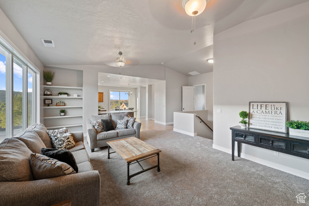 Carpeted living room with ceiling fan, a textured ceiling, built in features, and lofted ceiling