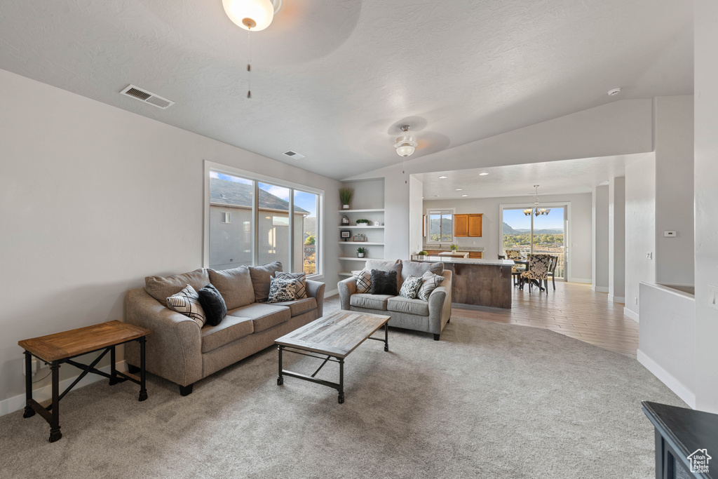 Carpeted living room featuring a textured ceiling, lofted ceiling, ceiling fan with notable chandelier, and built in shelves