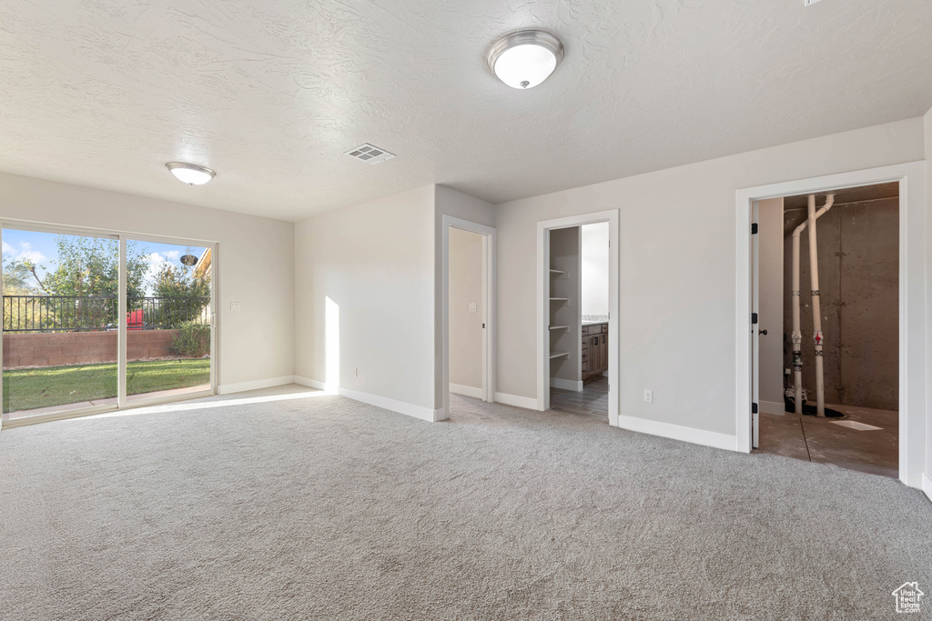 Unfurnished bedroom featuring carpet, a textured ceiling, a spacious closet, ensuite bathroom, and a closet