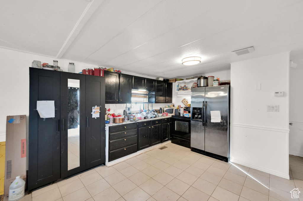 Kitchen with black / electric stove, light tile patterned floors, and stainless steel fridge