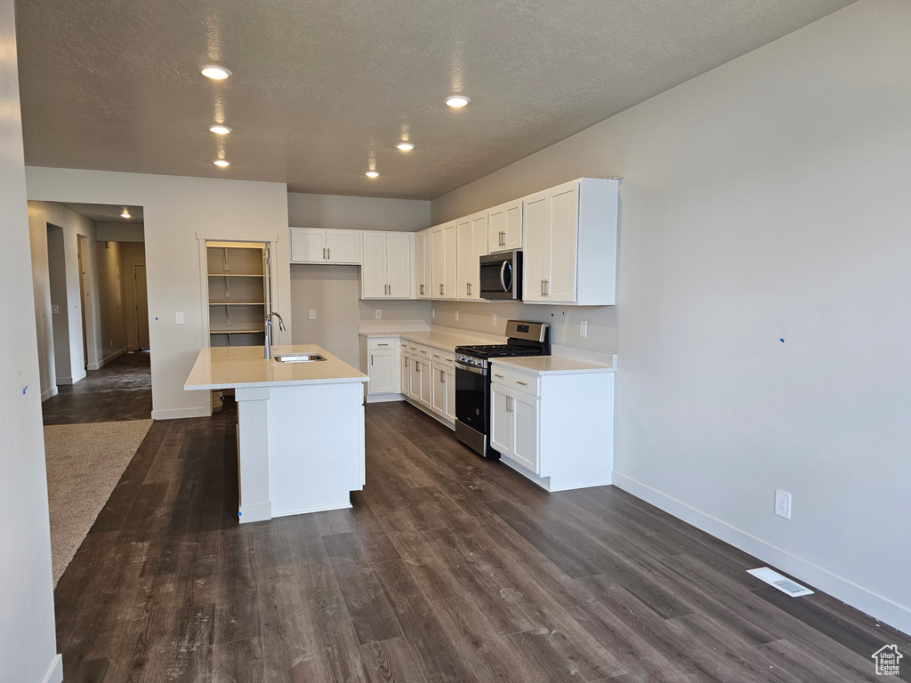 Kitchen featuring sink, dark hardwood / wood-style flooring, white cabinetry, stainless steel appliances, and a kitchen island with sink