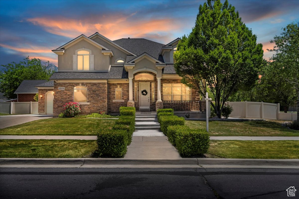 View of front of home featuring stucco siding, driveway, stone siding, and roof with shingles