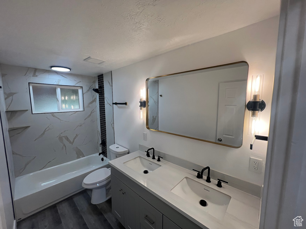 Full bathroom with tiled shower / bath, hardwood / wood-style floors, a textured ceiling, toilet, and vanity