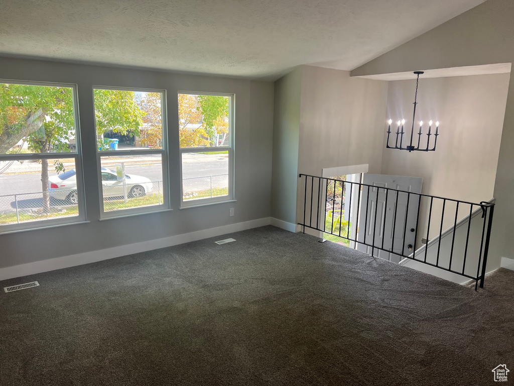 Spare room featuring vaulted ceiling, a textured ceiling, carpet floors, and a chandelier