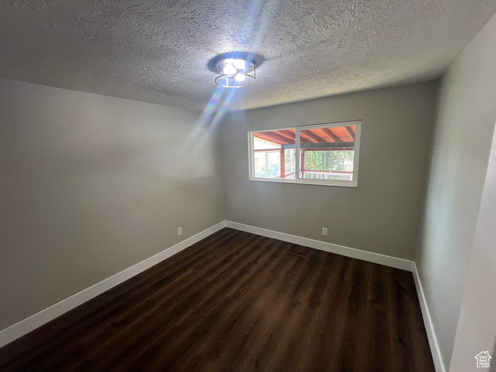 Unfurnished room with a textured ceiling and dark hardwood / wood-style flooring