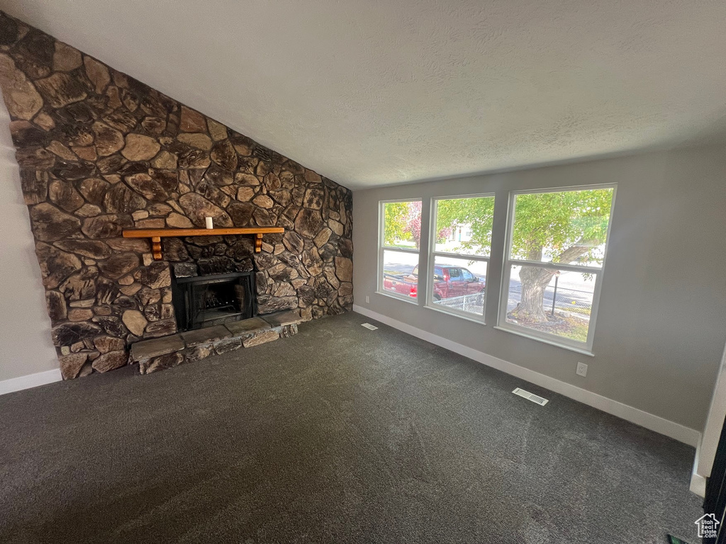 Unfurnished living room with carpet, a stone fireplace, and a textured ceiling