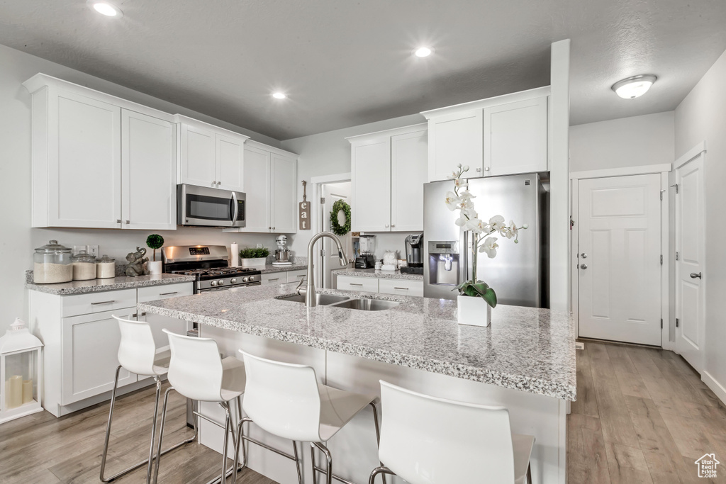 Kitchen with sink, light wood-type flooring, stainless steel appliances, white cabinets, and a kitchen island with sink