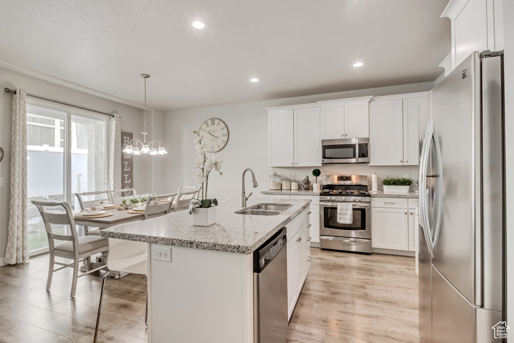 Kitchen with sink, hanging light fixtures, stainless steel appliances, white cabinets, and a center island with sink