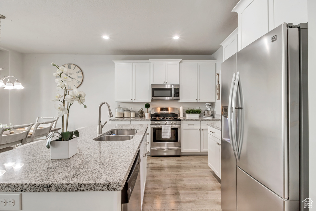 Kitchen with a kitchen island with sink, sink, white cabinets, light wood-type flooring, and appliances with stainless steel finishes