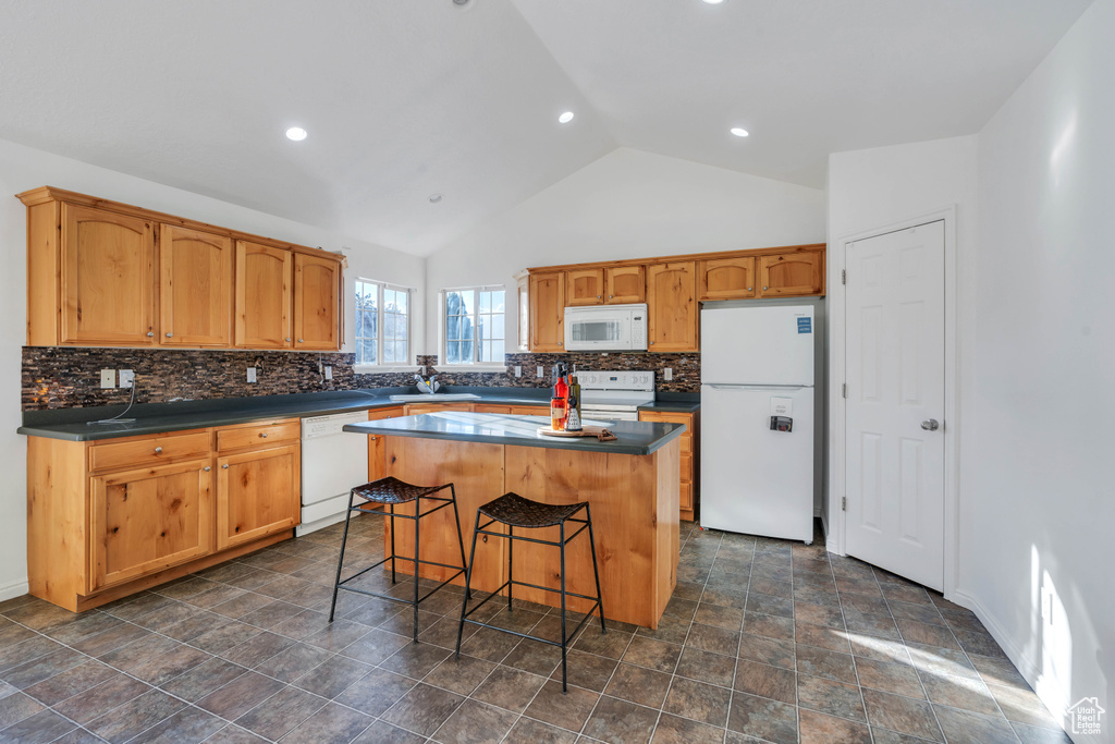 Kitchen featuring a kitchen island, decorative backsplash, a breakfast bar area, white appliances, and high vaulted ceiling