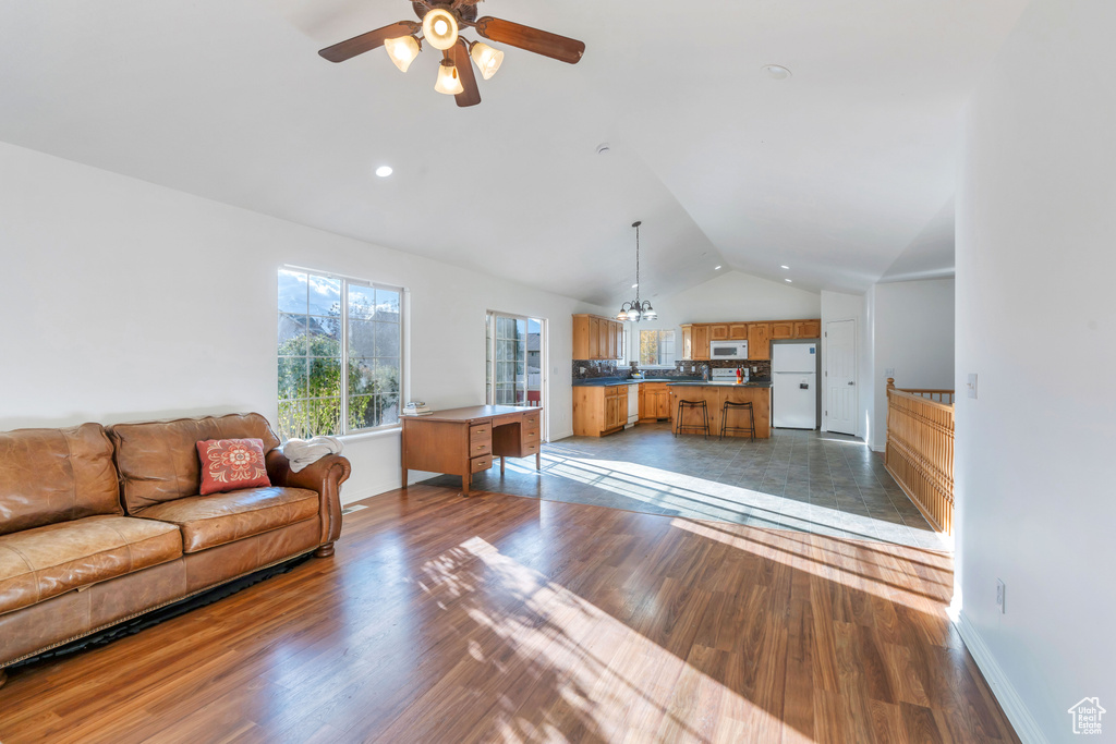 Living room with ceiling fan with notable chandelier, vaulted ceiling, and dark hardwood / wood-style floors