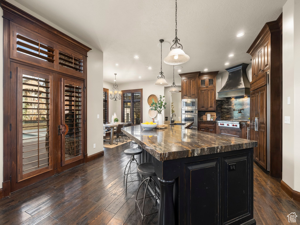 Kitchen featuring a spacious island, dark hardwood / wood-style flooring, custom exhaust hood, and hanging light fixtures