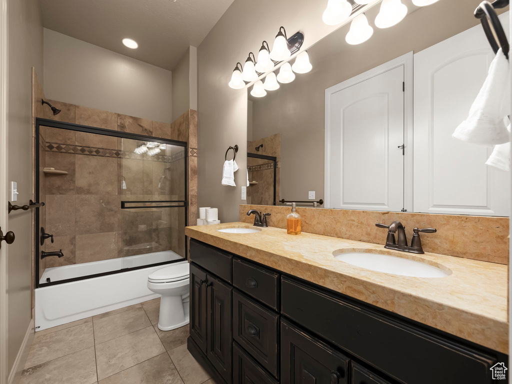 Full bathroom featuring vanity, bath / shower combo with glass door, toilet, and tile patterned flooring