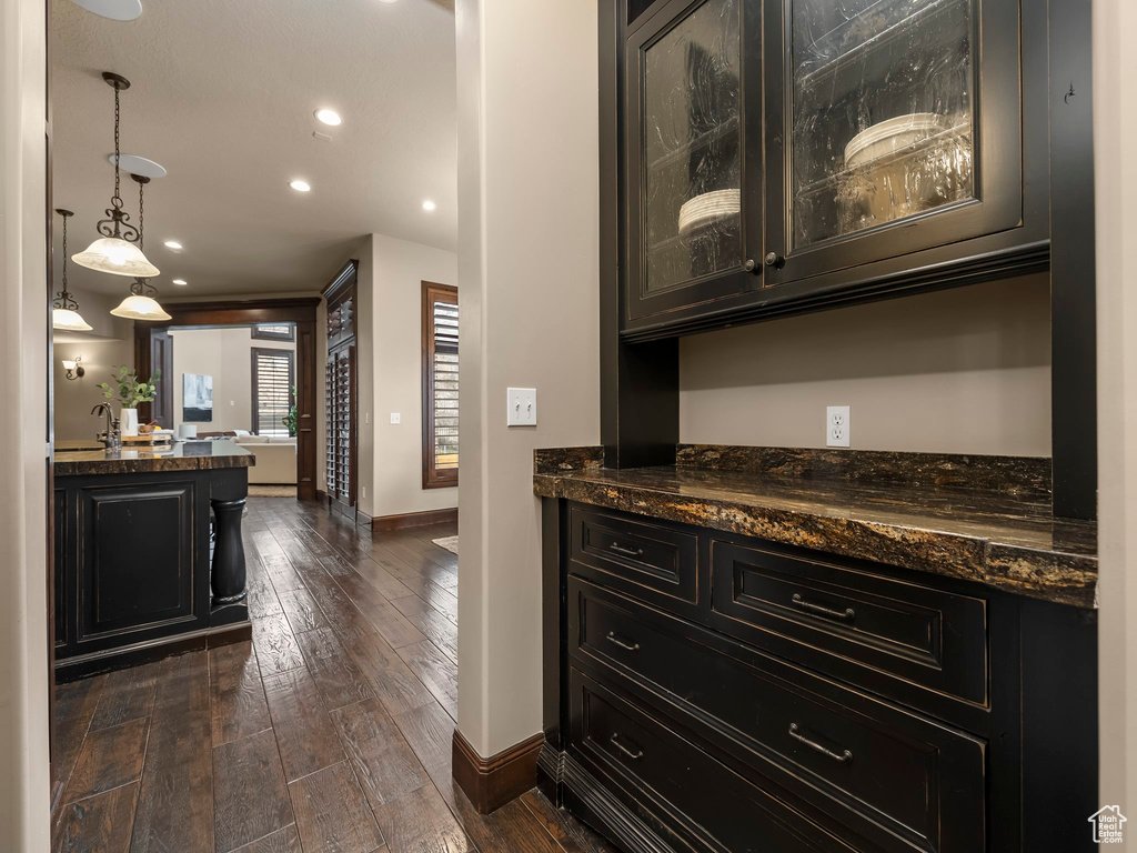 Bar featuring decorative light fixtures, dark wood-type flooring, and dark stone counters