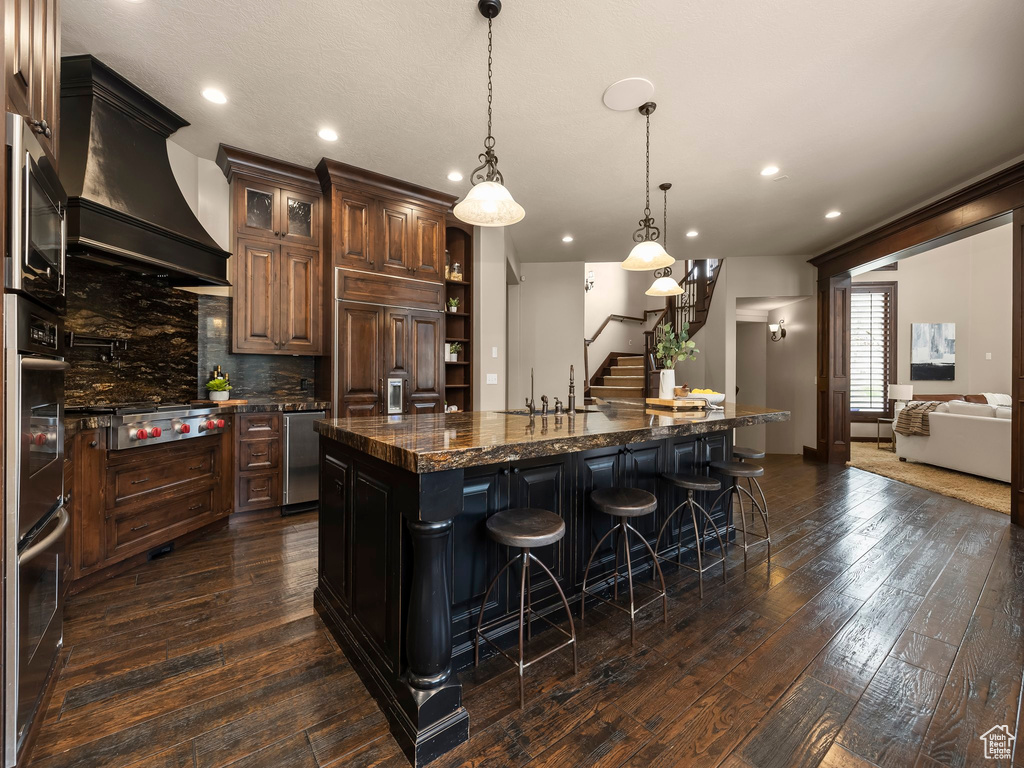 Kitchen featuring custom exhaust hood, stainless steel appliances, dark wood-type flooring, and a large island