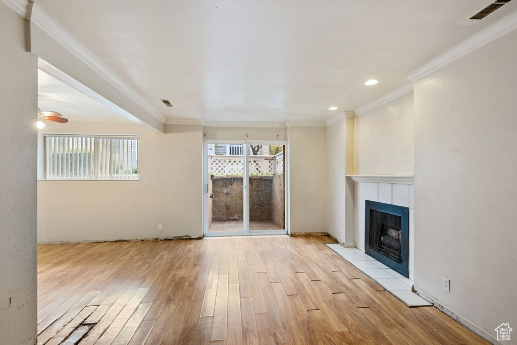 Unfurnished living room with ornamental molding, a tiled fireplace, light wood-type flooring, and ceiling fan