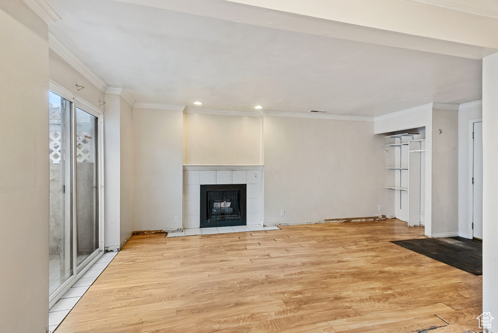 Unfurnished living room with a tiled fireplace, crown molding, and light hardwood / wood-style flooring