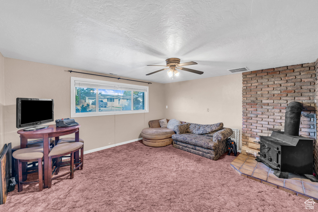 Carpeted living room with a textured ceiling, a wood stove, and ceiling fan