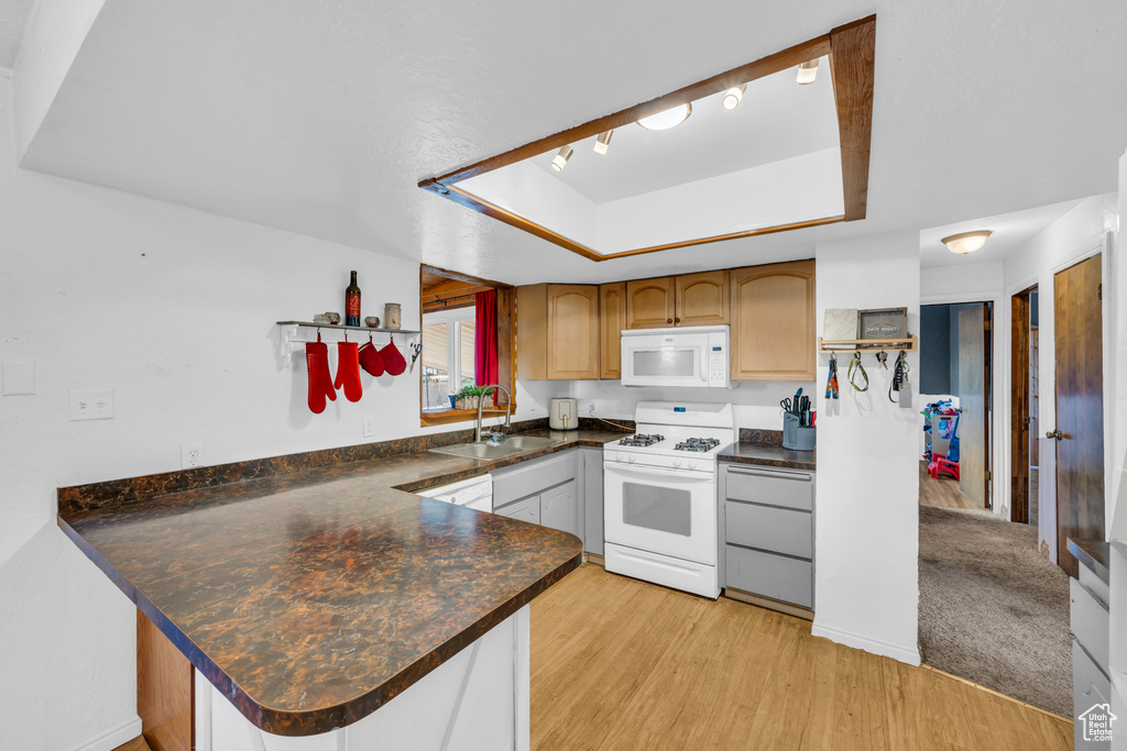 Kitchen with sink, kitchen peninsula, white appliances, and a raised ceiling