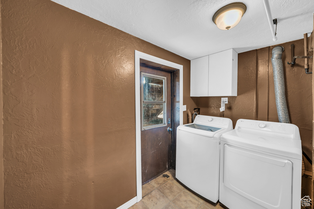 Laundry room featuring independent washer and dryer, light tile patterned flooring, a textured ceiling, and cabinets