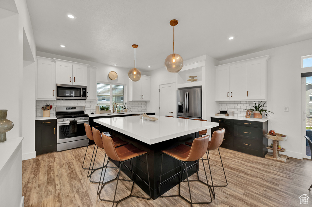 Kitchen featuring appliances with stainless steel finishes, white cabinets, a kitchen island, and pendant lighting