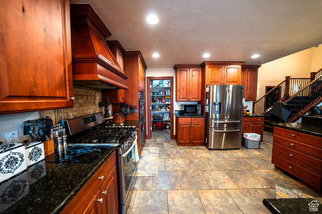 Kitchen featuring premium range hood, appliances with stainless steel finishes, dark stone countertops, and tasteful backsplash