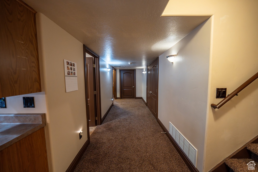 Corridor featuring a textured ceiling and dark colored carpet