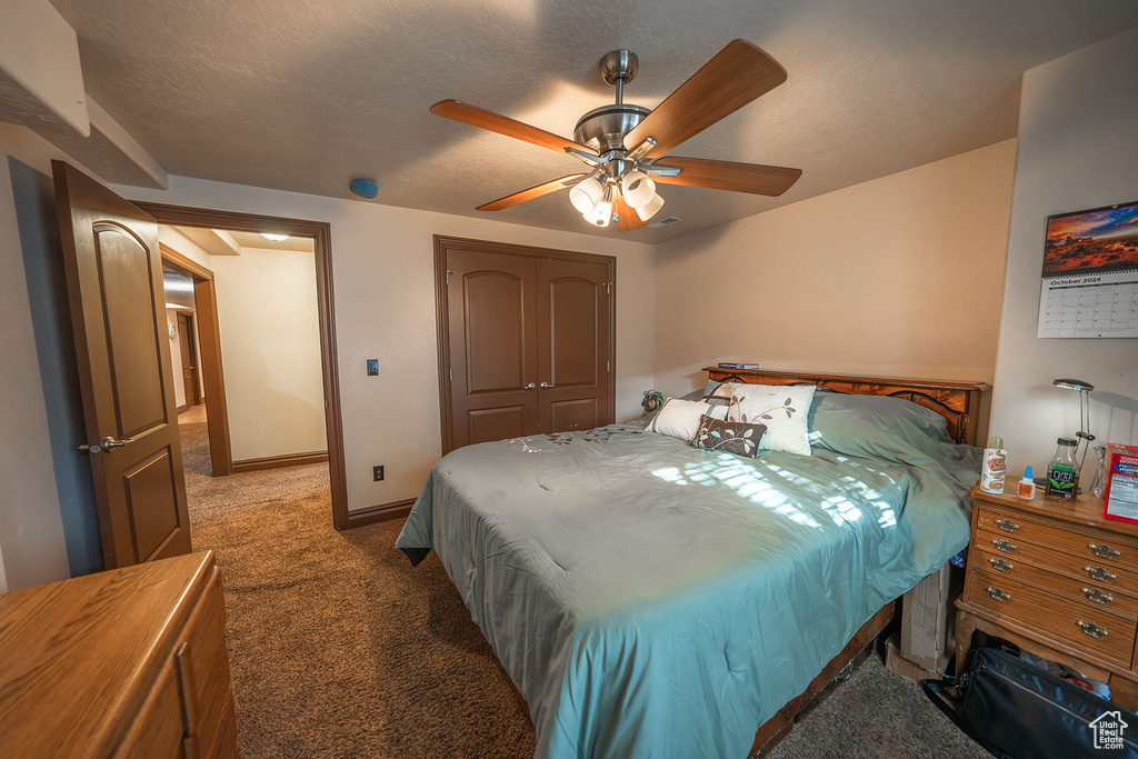 Carpeted bedroom with a closet, ceiling fan, and a textured ceiling