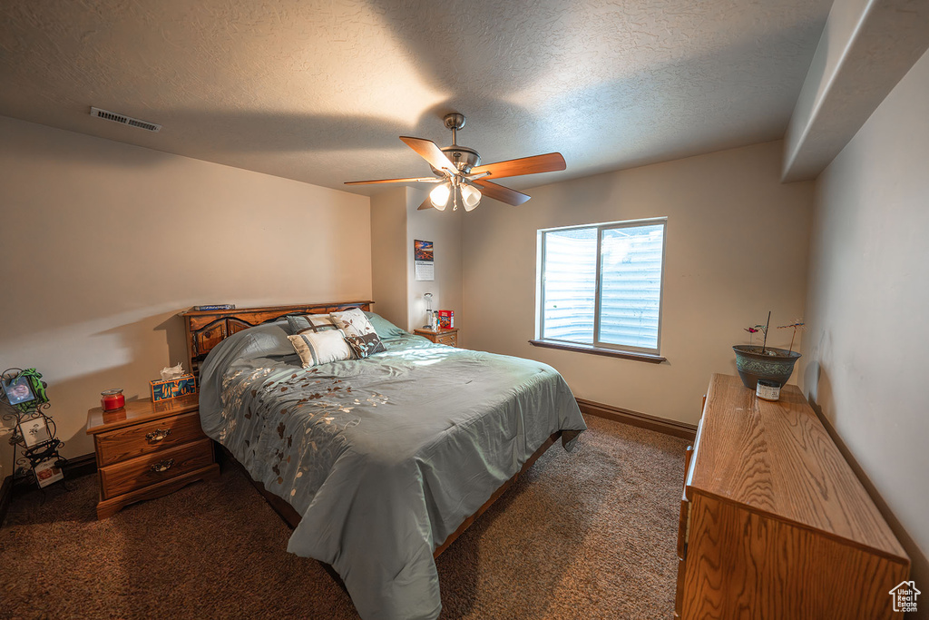 Bedroom featuring ceiling fan, a textured ceiling, and dark carpet