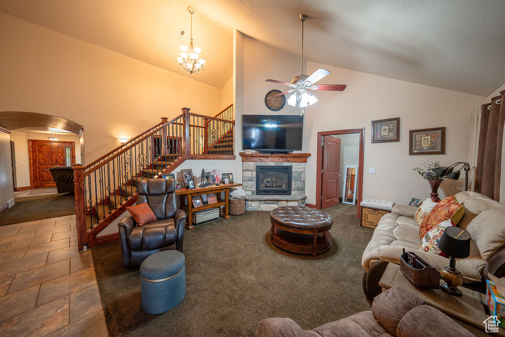 Living room with ceiling fan with notable chandelier, dark colored carpet, a fireplace, and high vaulted ceiling