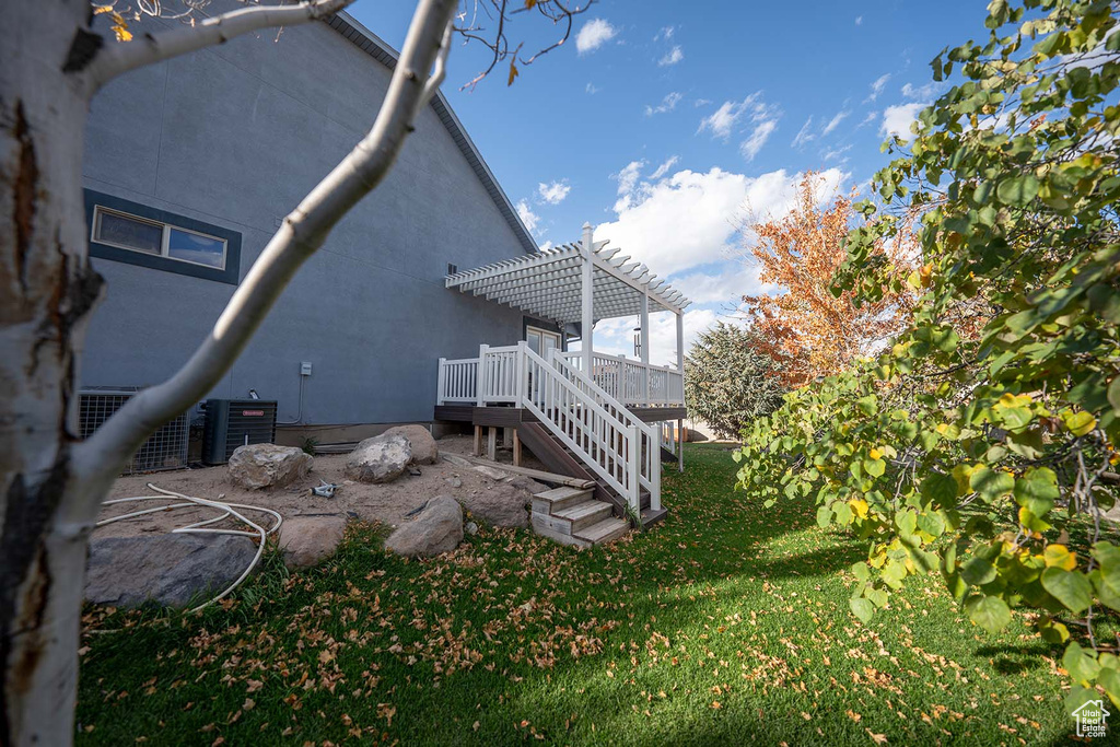 Exterior space featuring a deck, a lawn, central AC unit, and a pergola