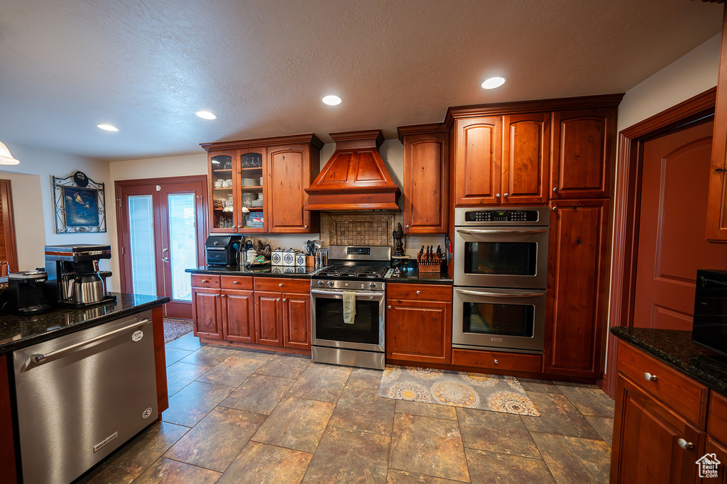 Kitchen with appliances with stainless steel finishes, french doors, a textured ceiling, dark stone countertops, and premium range hood