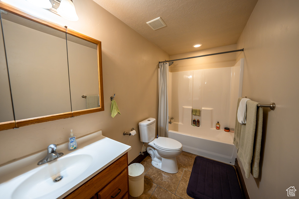 Full bathroom with a textured ceiling, toilet, vanity, shower / tub combo with curtain, and tile patterned flooring