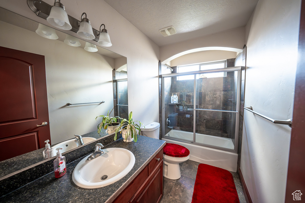 Full bathroom featuring vanity, enclosed tub / shower combo, a textured ceiling, and toilet