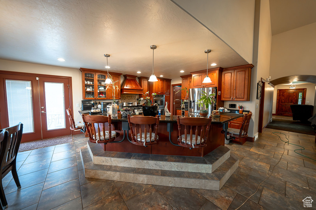 Kitchen with stainless steel appliances, pendant lighting, custom exhaust hood, decorative backsplash, and a breakfast bar area